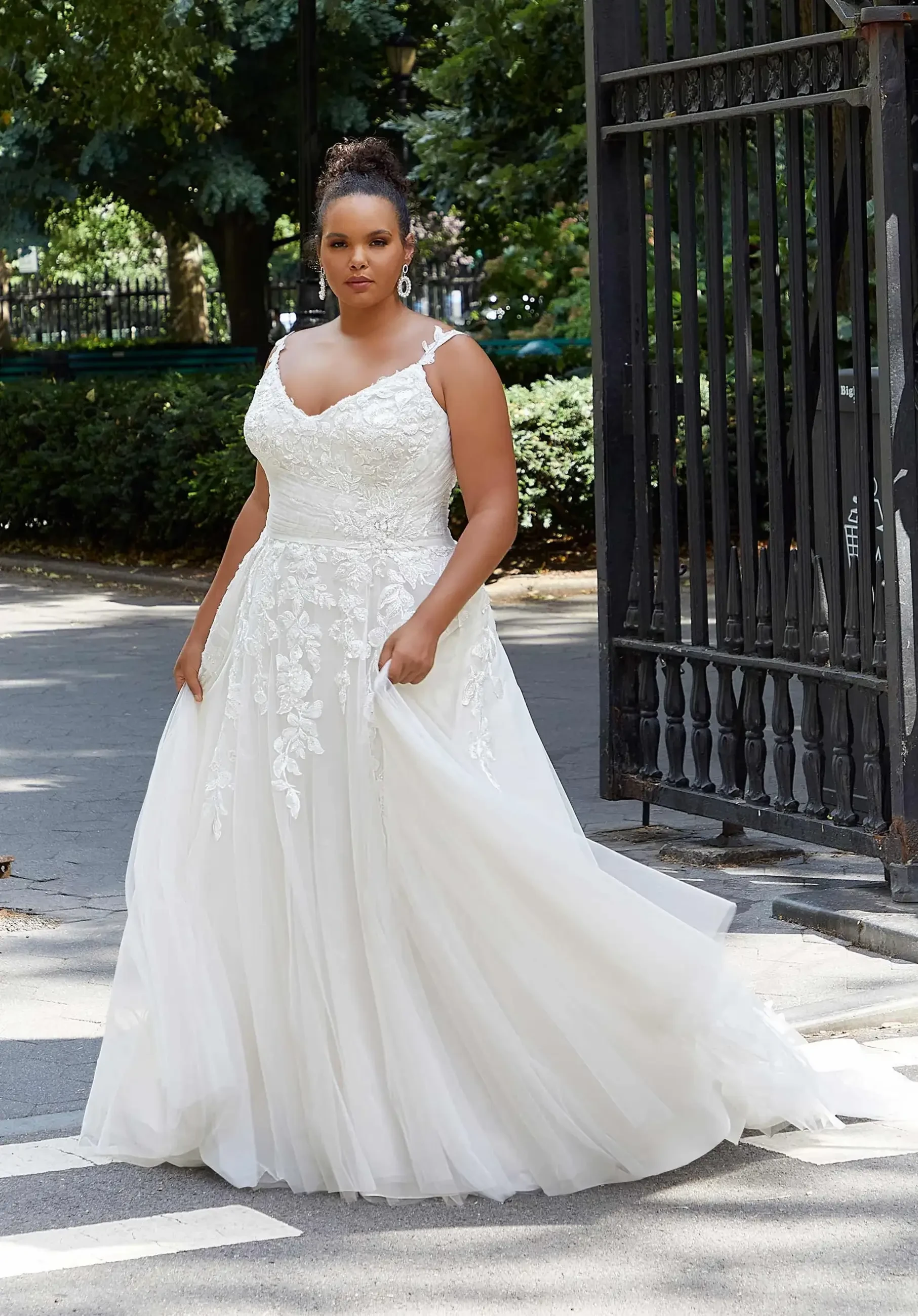 Model is wearing a plus size ball gown wedding dress with frosted lace appliques, plunging neckline, and tulle skirt