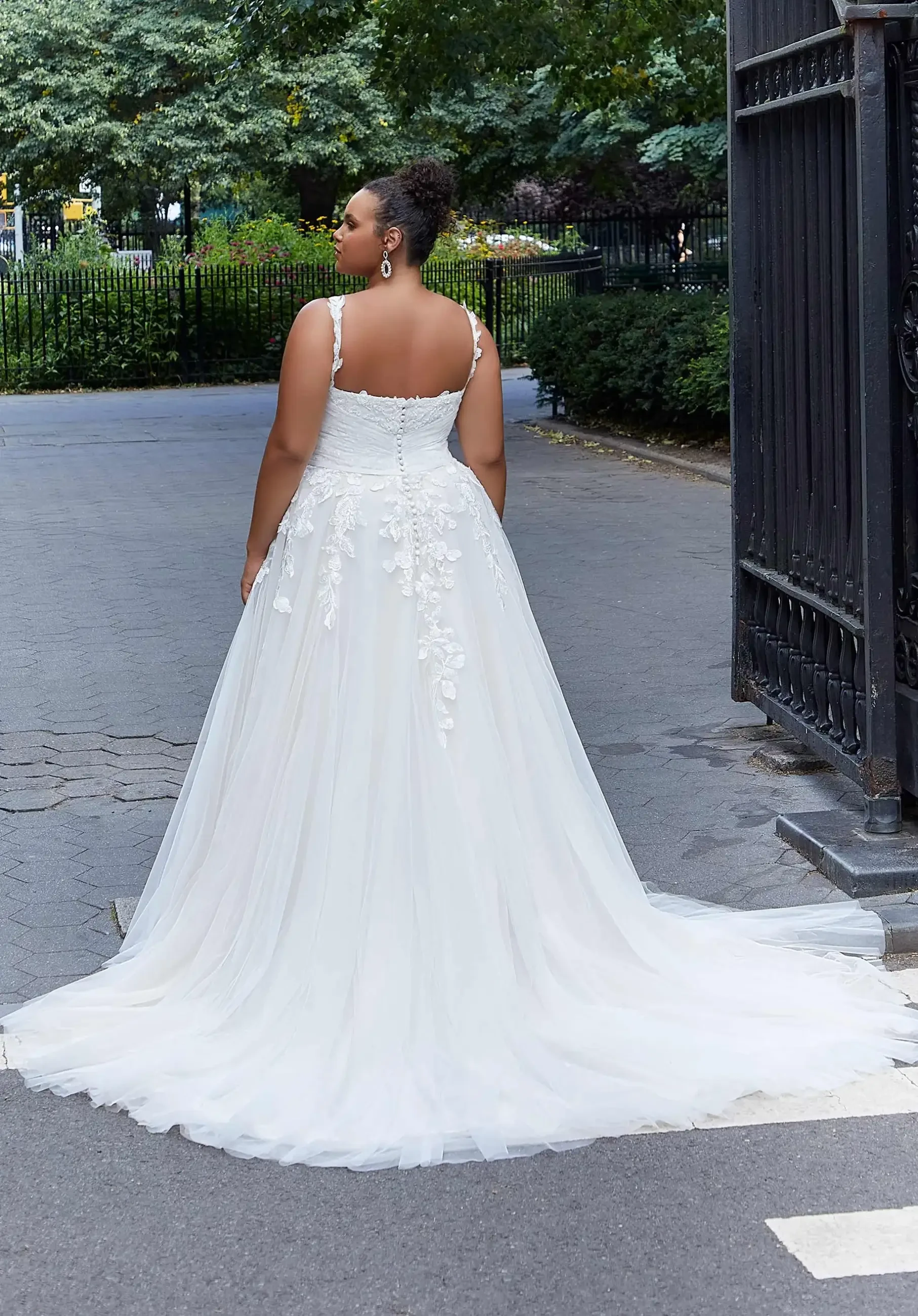 Model is wearing a plus size ball gown wedding dress with frosted lace appliques, plunging neckline, and tulle skirt