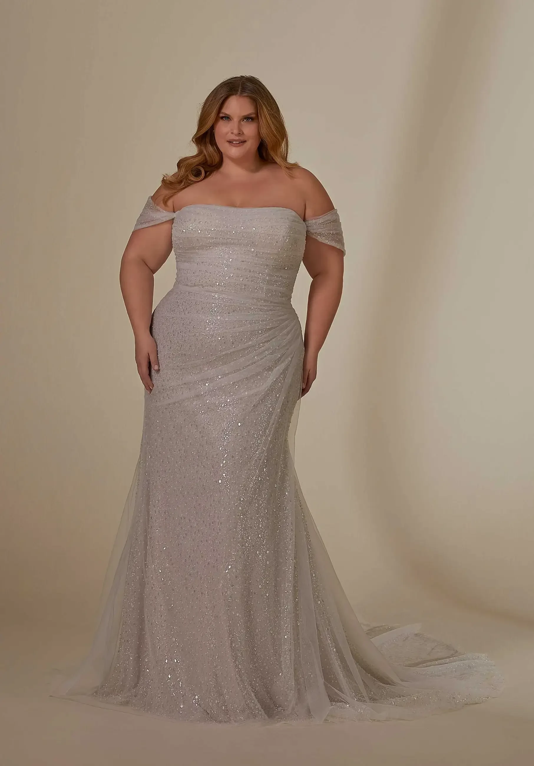 Model is wearing a fit and flare plus size wedding dress with a draped tulle overlay and detachable sleeves