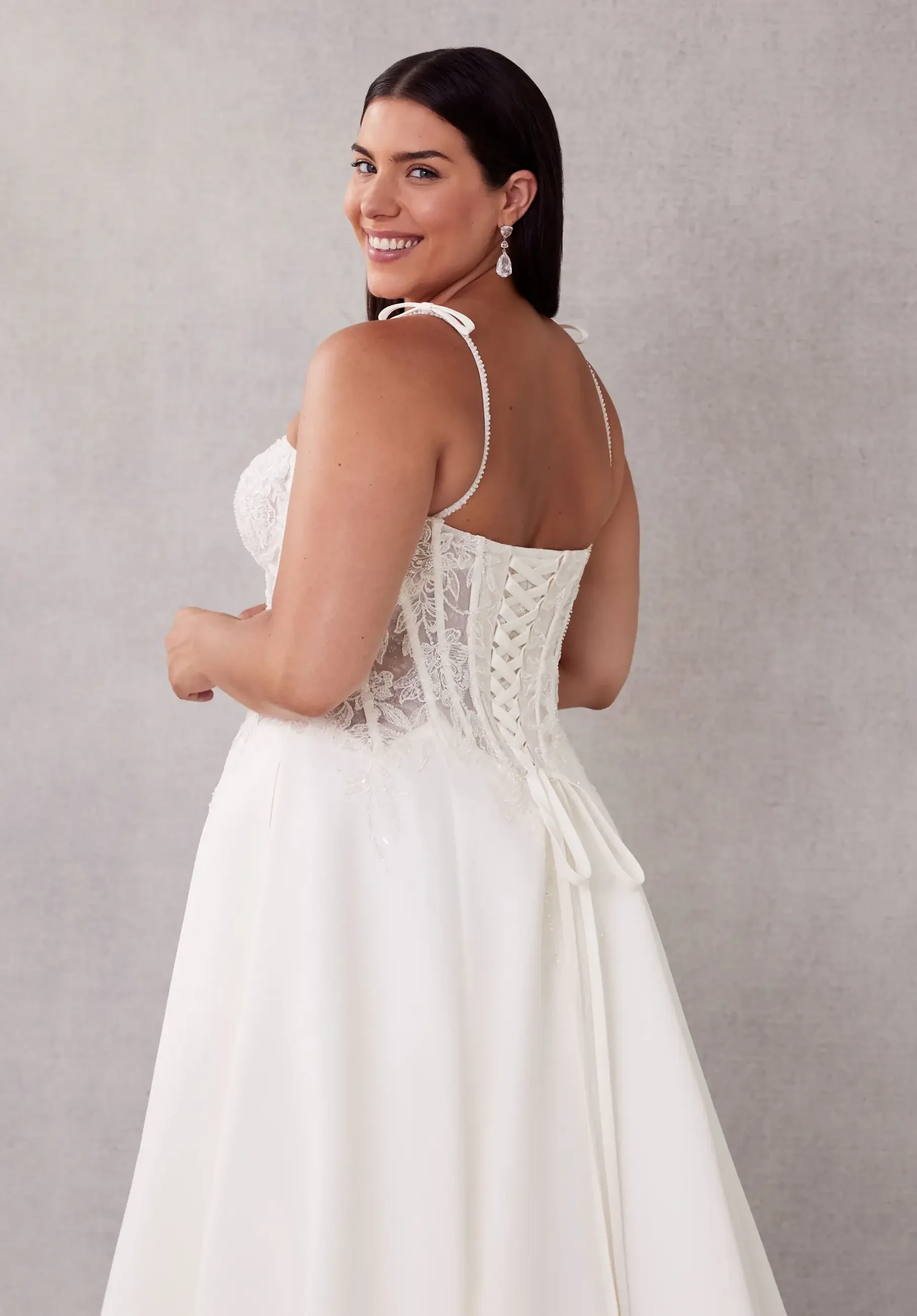 Model is wearing an a-line plus size bridal gown with a lace up corset back and sweetheart neckline