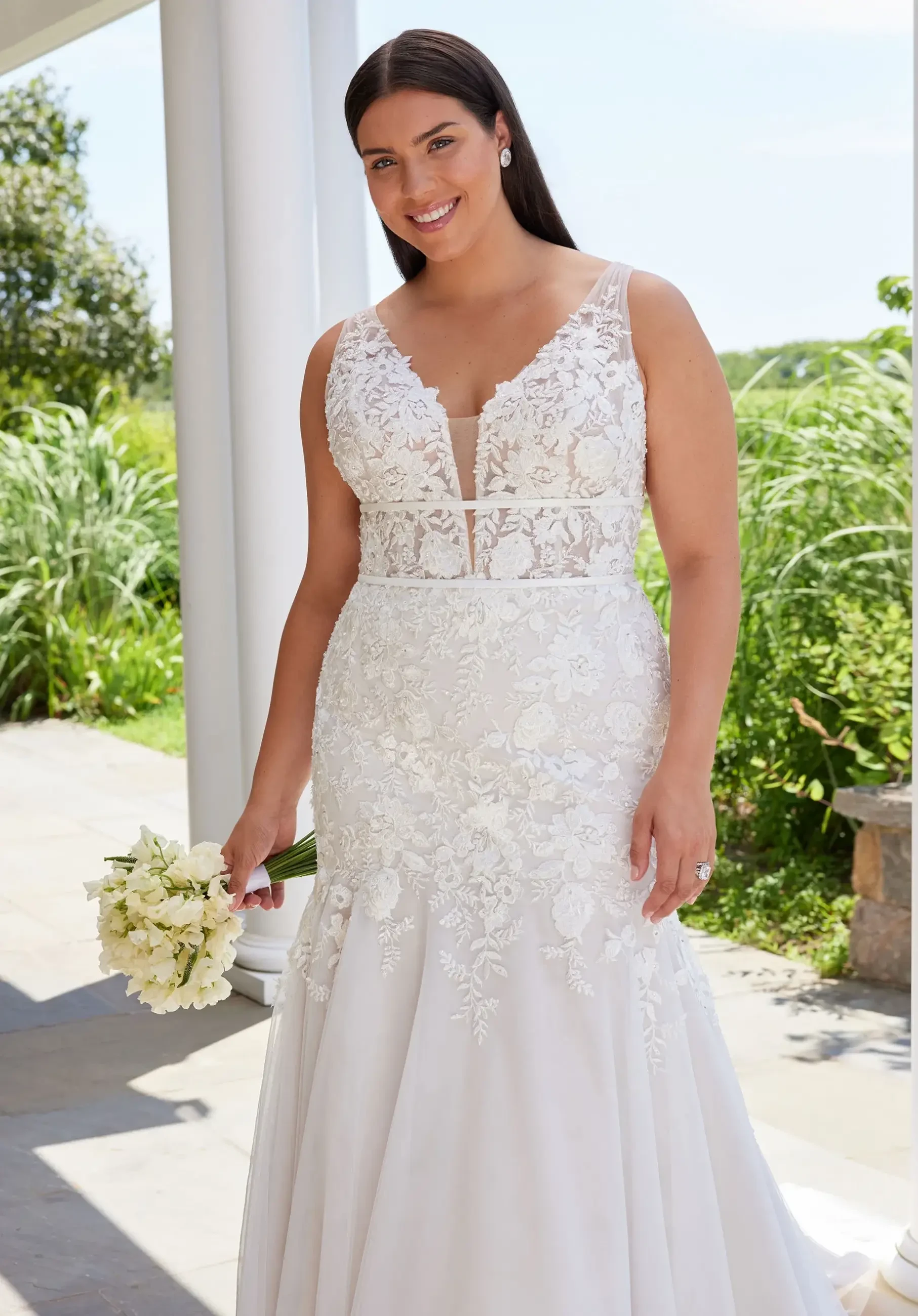 Model is wearing a mermaid plus size wedding dress with soft tulle and crystal beaded floral lace