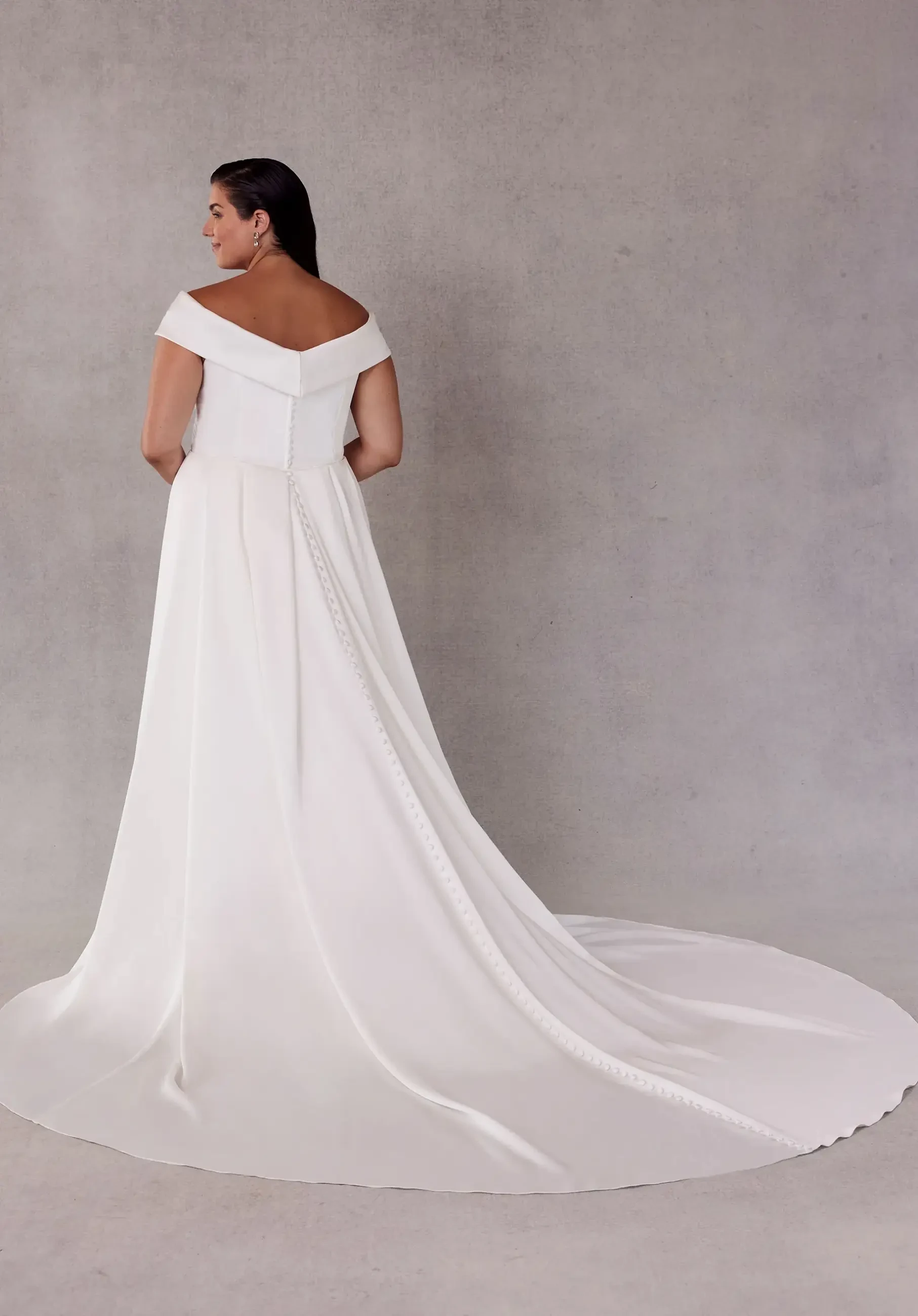 model is wearing an off the shoulder sheath plus size bridal gown