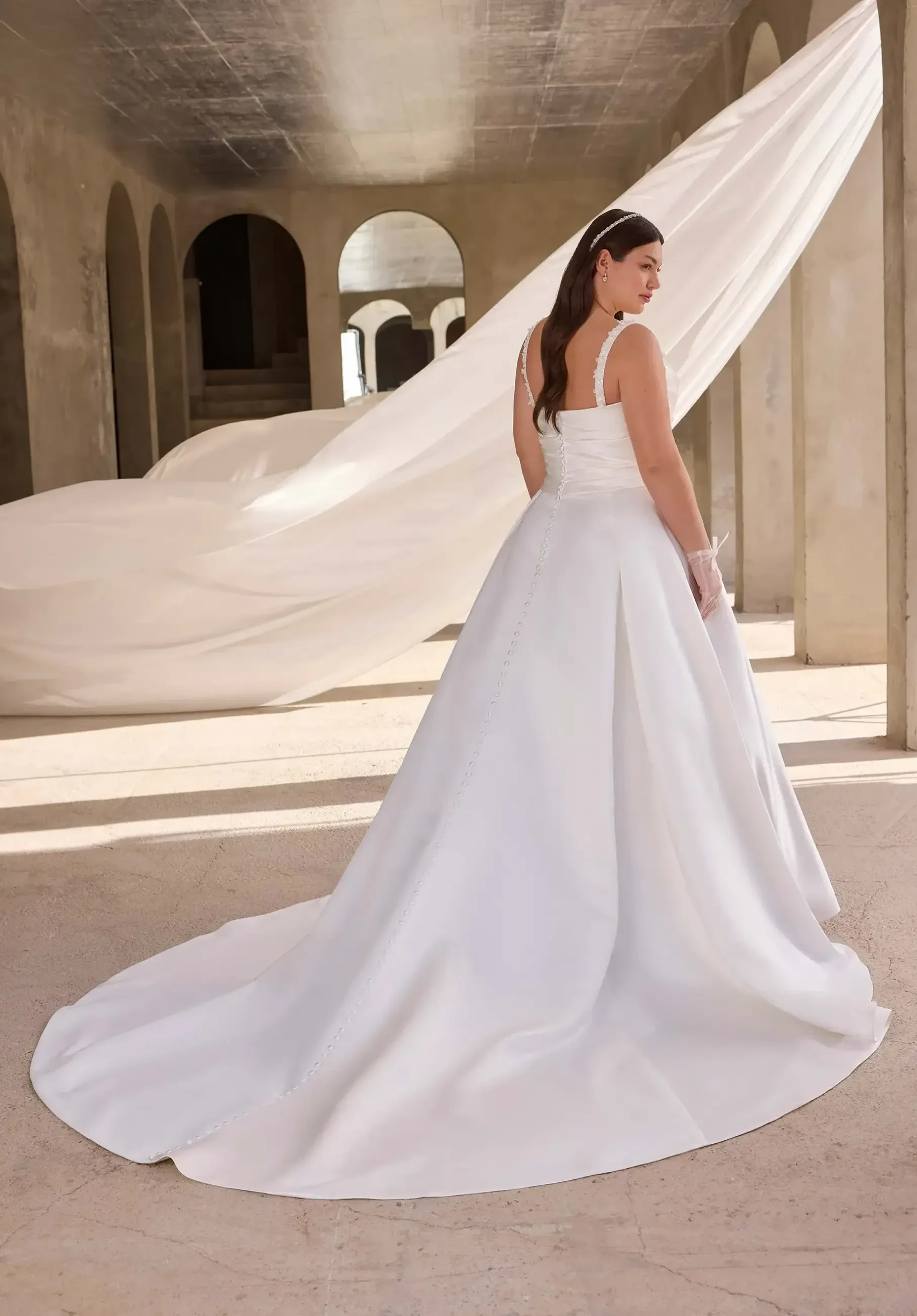 model is wearing a sleeveless a-line plus size wedding dress with a train