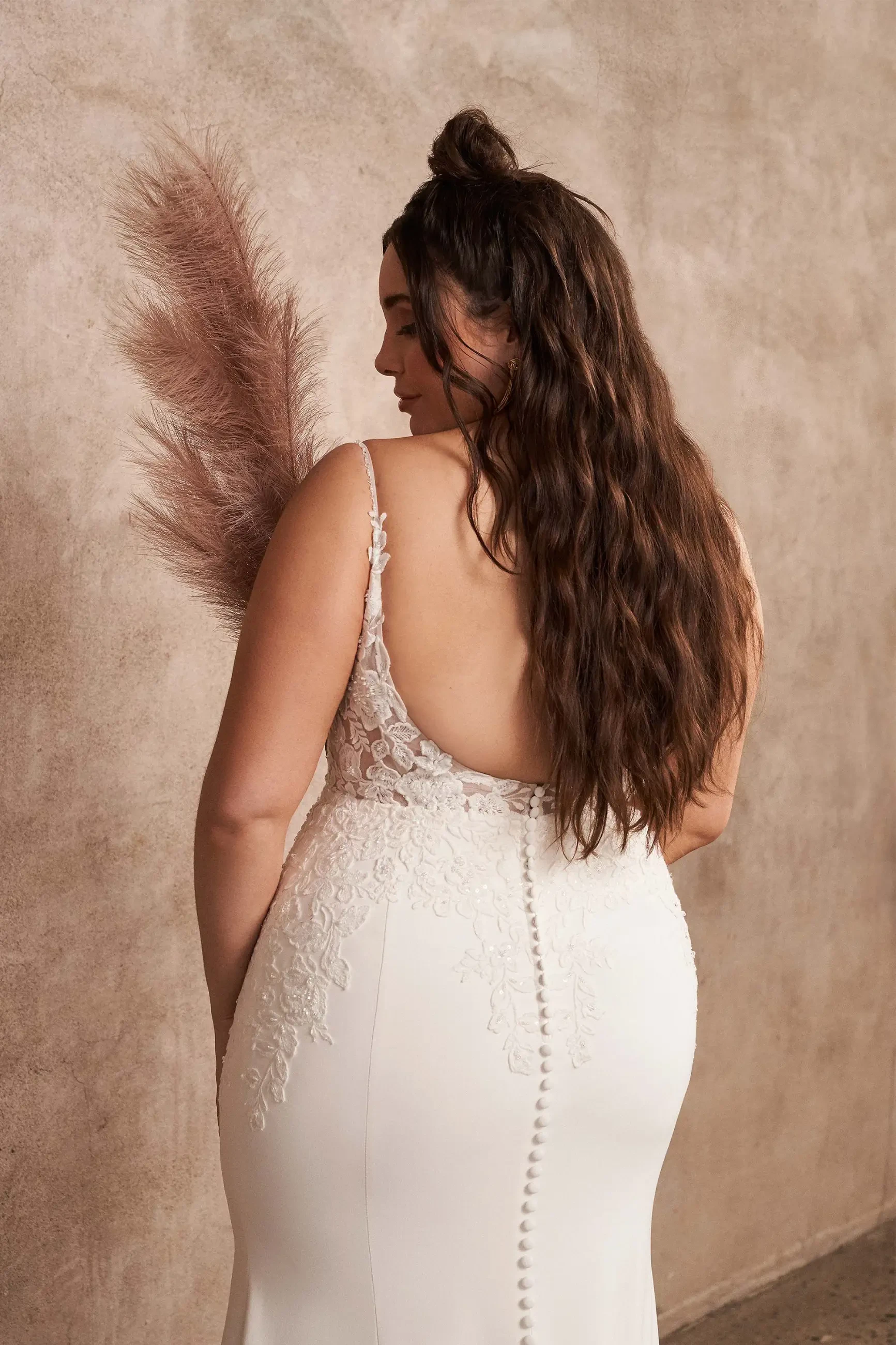 Model is wearing a crepe plus size fit and flare wedding dress with beaded floral appliques and an open back with a chapel train