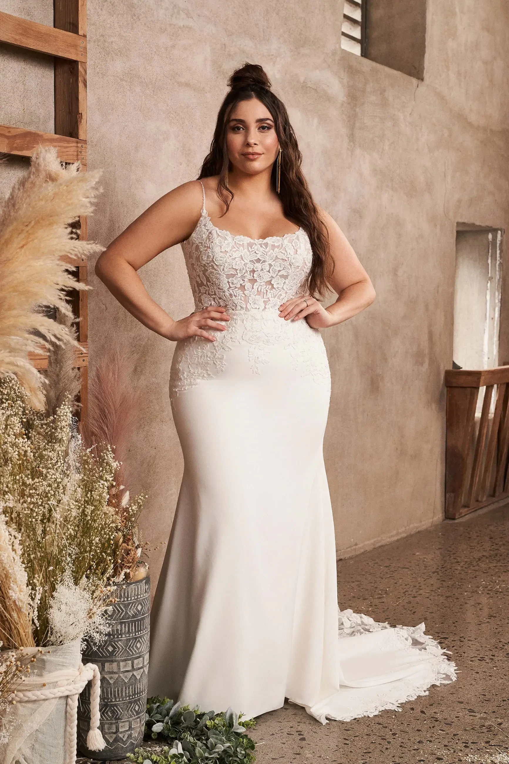Model is wearing a crepe plus size fit and flare wedding dress with beaded floral appliques and an open back with a chapel train