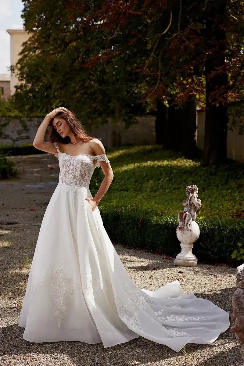 model is wearing an off the shoulder a-line wedding gown