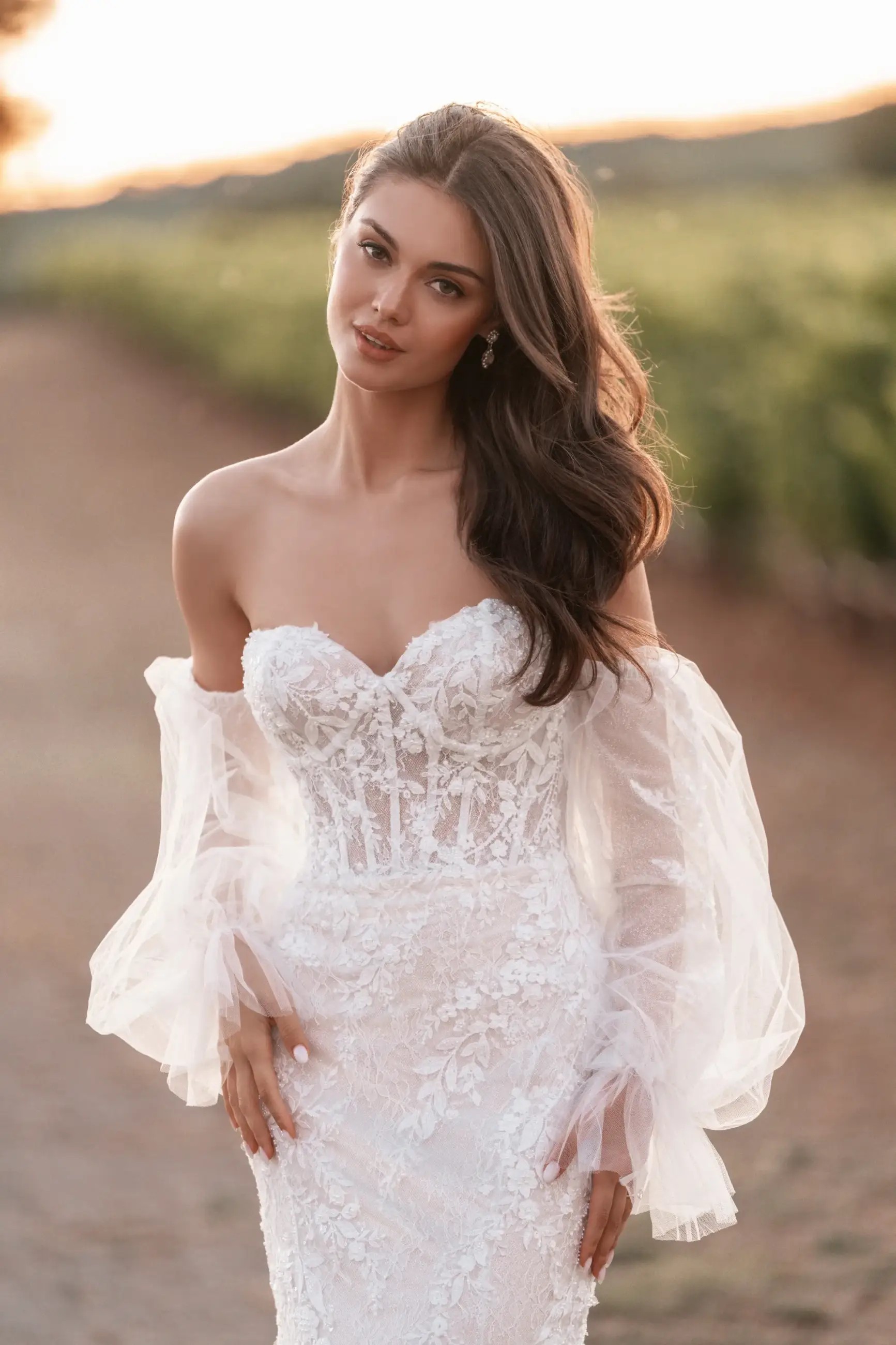 Model is wearing a strapless fitted bridal gown with detachable puff sleeves
