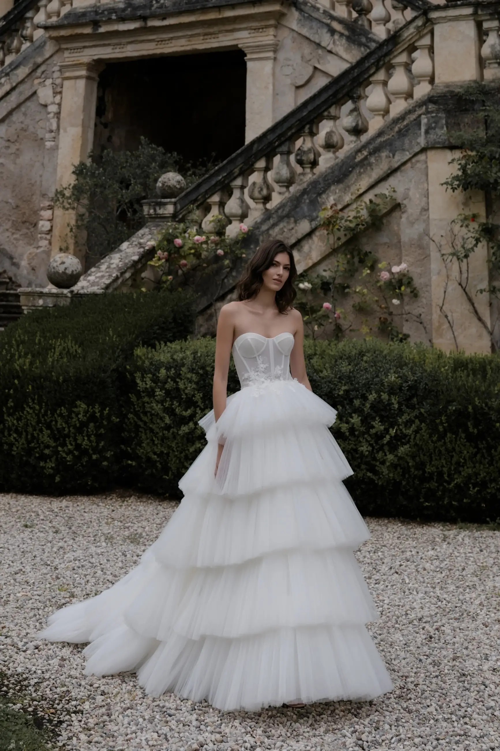 Model is wearing a strapless ball gown wedding dress with a tiered tulle skirt