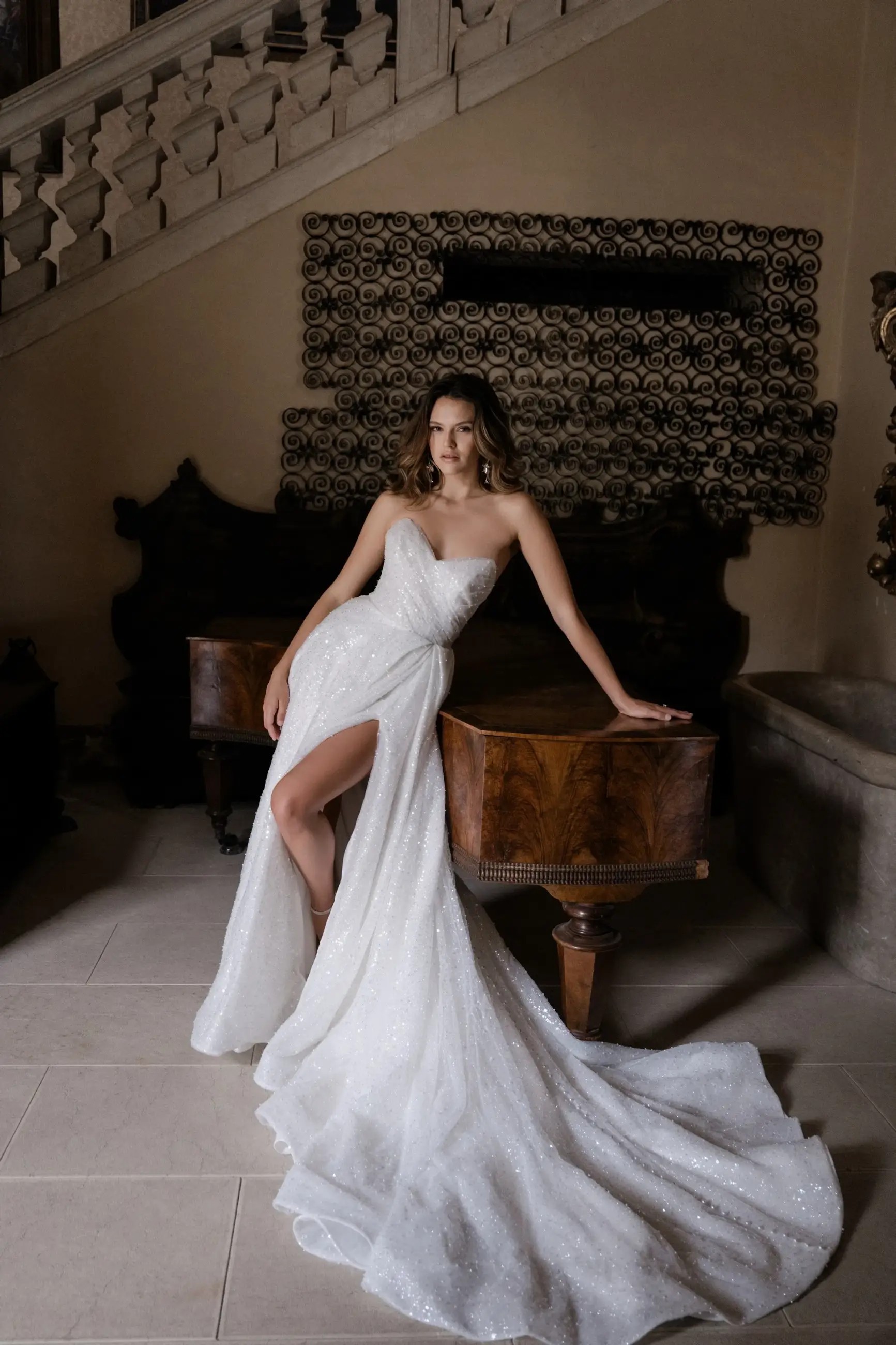 Model is wearing a strapless a-line gown with a high slit and a long train