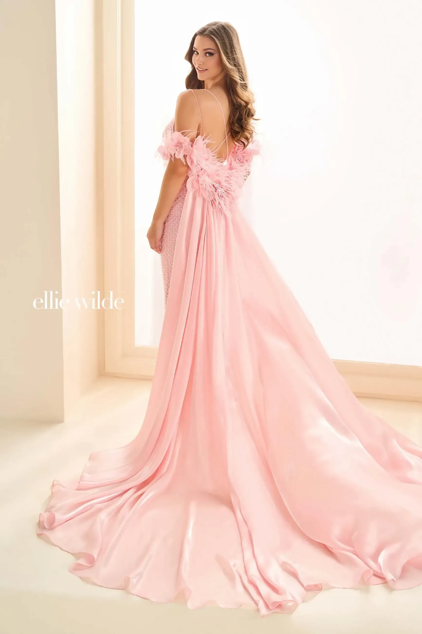 model is wearing a light pink off the shoulder prom dress with feather accents