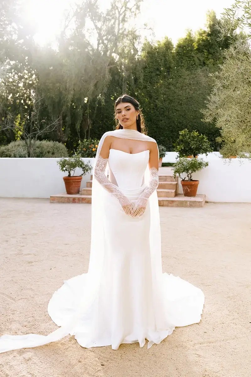 Model is wearing a strapless fit and flare bridal gown with a chiffon neck scarf draped around her neck and trailing down the back